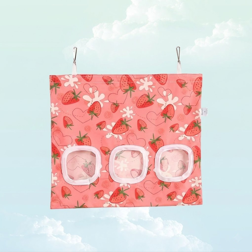 Front view of a pink strawberry print hanging hay bag for guinea pigs with three feeding windows