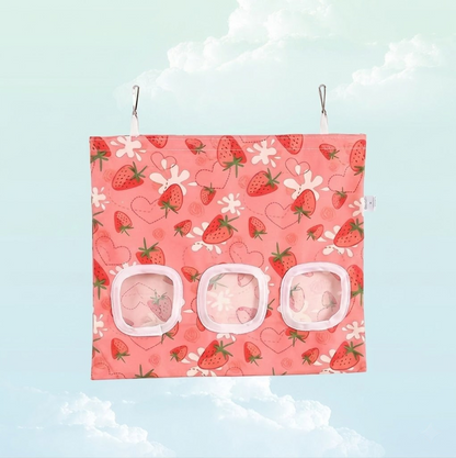 Front view of a pink strawberry print hanging hay bag for guinea pigs with three feeding windows